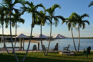 A lakeside patio with lounge chairs, umbrellas, and a dock. - Serenity Bay Cottages (Matlacha)