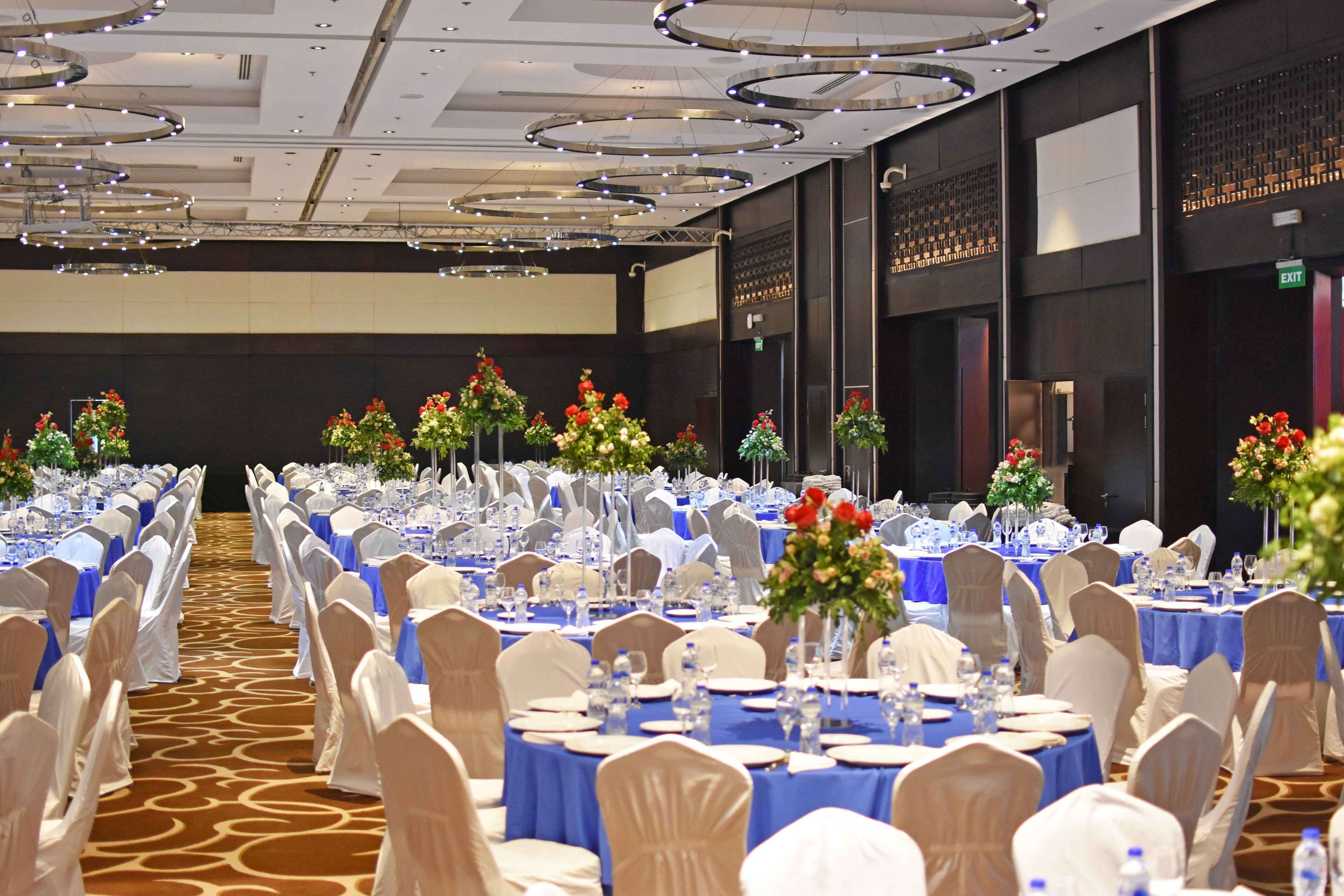 A banquet hall with round tables set for dining, white chairs, and blue tablecloths.