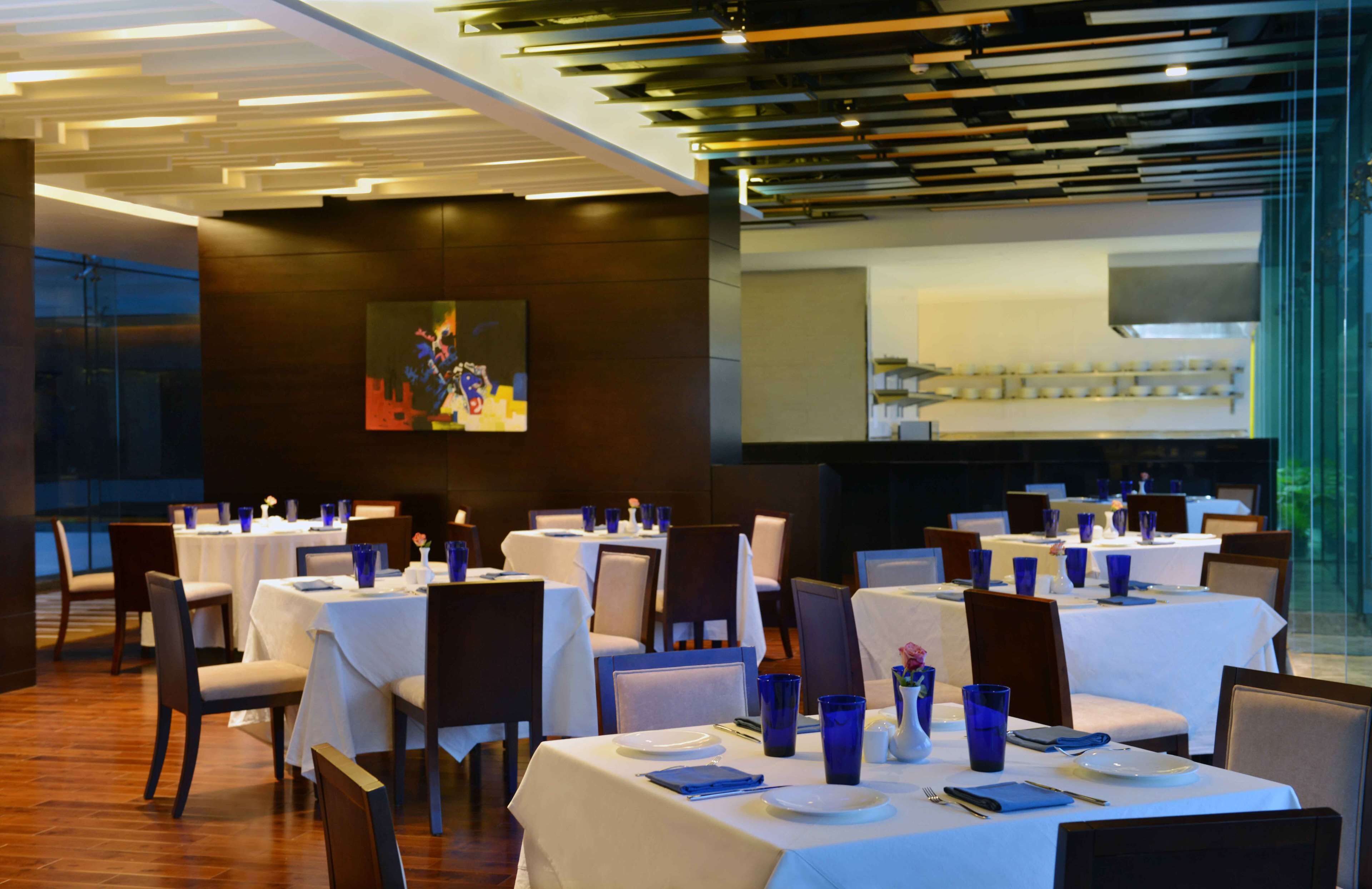 A restaurant with multiple tables set for dining, featuring a modern interior with wooden floors and a large painting on the wall.