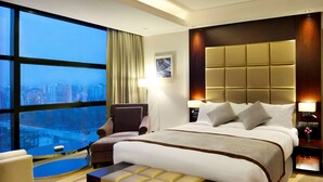 A modern hotel room with a large bed, a sitting area, and a view of a cityscape. - Radisson Blu Chattogram Bay View (Chittagong)