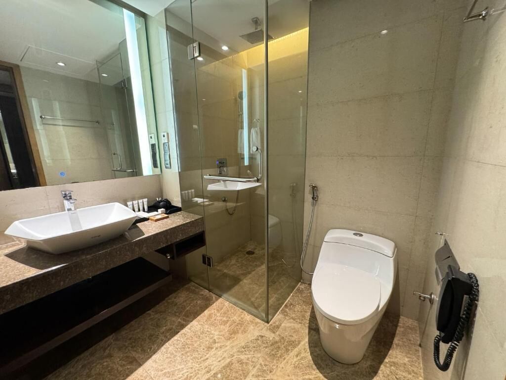 Un baño moderno con un espejo grande, dos lavamanos, un inodoro y una zona de ducha con paredes de vidrio.