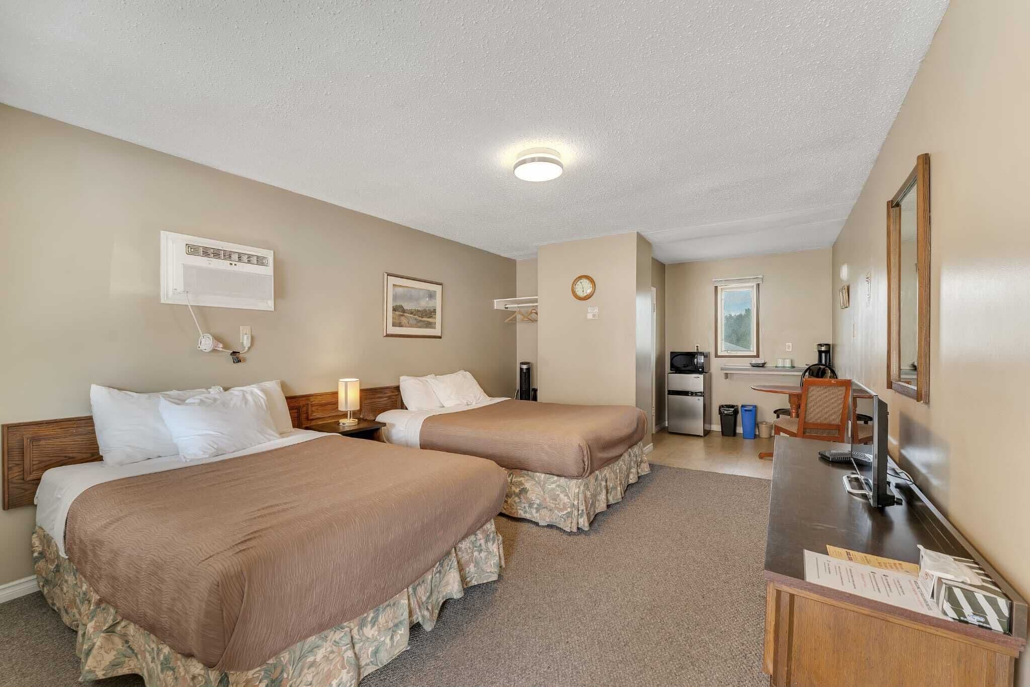 A hotel room with two beds, a desk, a coffee maker, a clock, and a mirror.