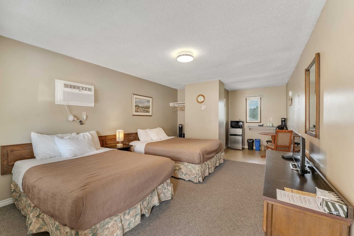 A hotel room with two beds, a desk, a coffee maker, a clock, and a mirror.