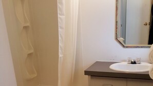 A bathroom with a bathtub, a sink, a toilet, and a mirror. - Badlands Motel (Drumheller)