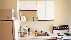A compact kitchen with white cabinets, a refrigerator, a stove, and a sink. - Badlands Motel (Drumheller)