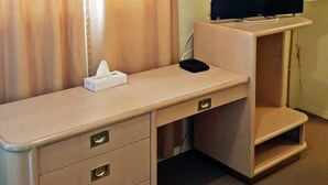 A room with a desk, a television, a lamp, and a curtain. - Badlands Motel (Drumheller)