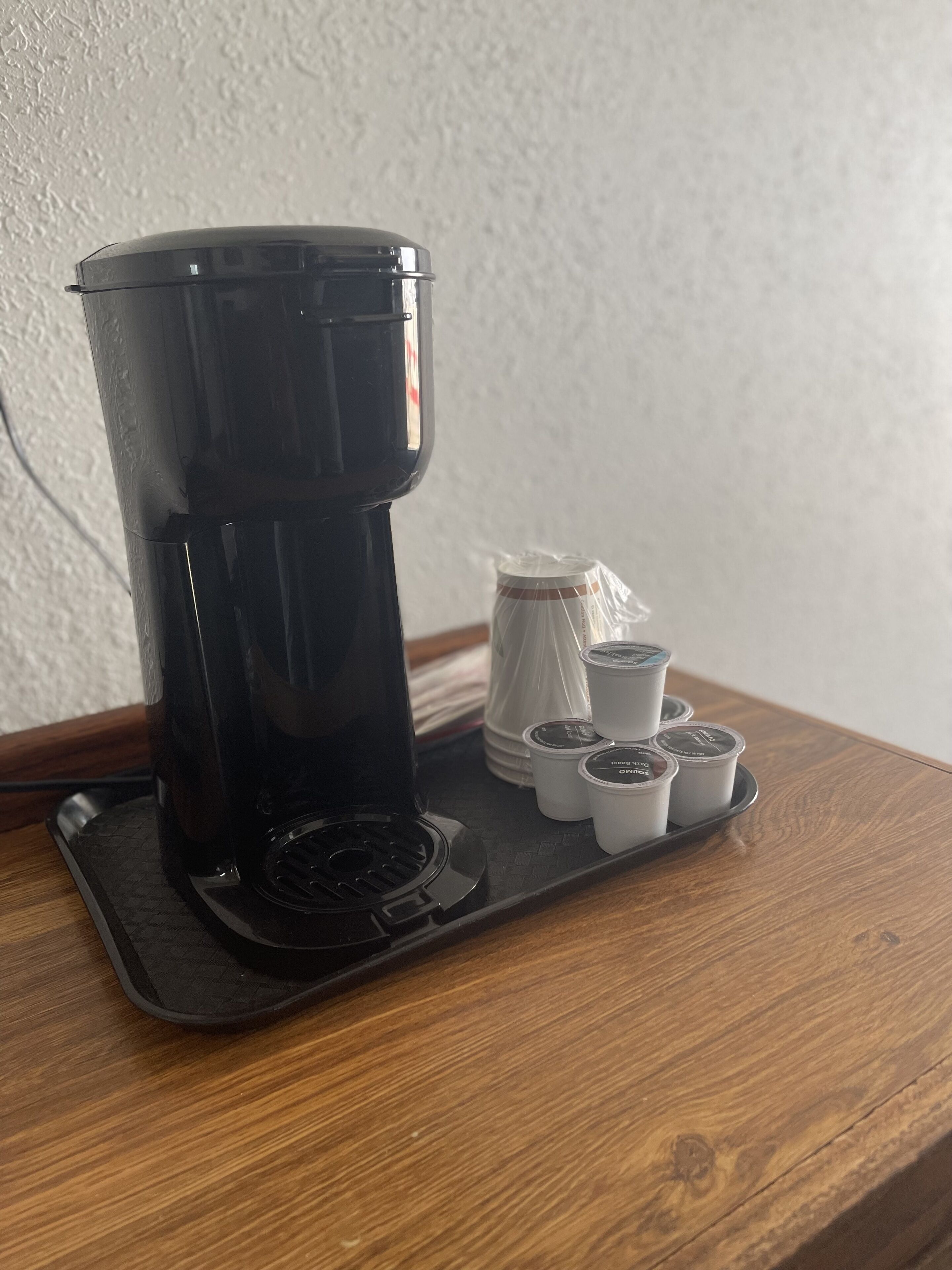 A coffee maker with a tray of disposable cups on a wooden table.