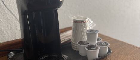 A coffee maker with a tray of disposable cups on a wooden table.