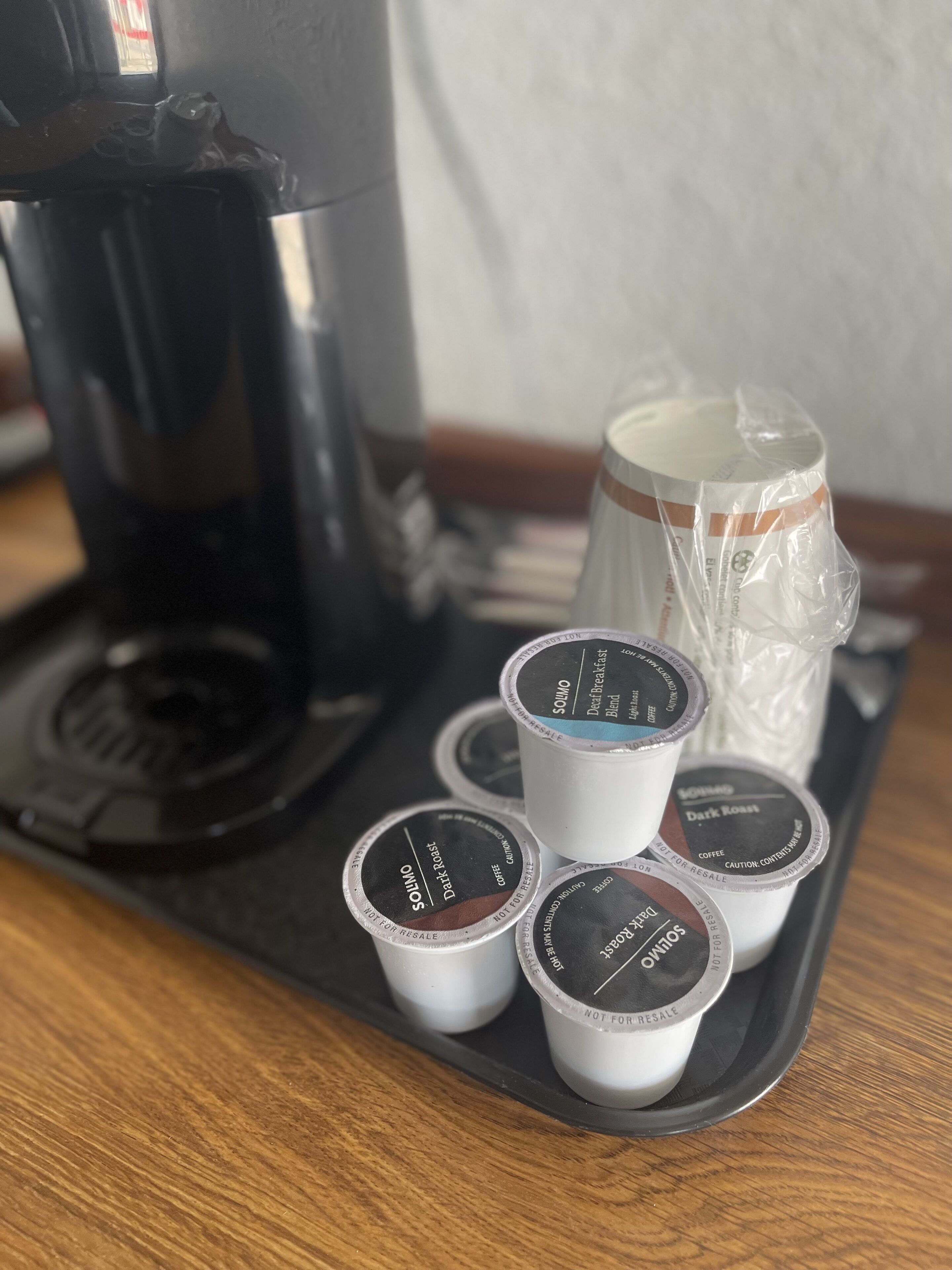 A tray with coffee pods and a coffee maker on a wooden table.