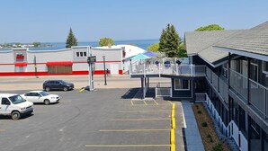 A parking lot with marked spaces, a building with a red and white facade, and a view of the sea in the background. - Bayside Inn  (St Ignace)