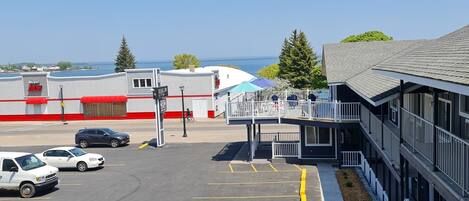 A parking lot with marked spaces, a building with a red and white facade, and a view of the sea in the background.
