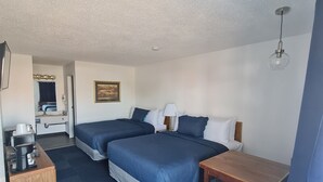 A hotel room with two beds, a wooden desk with a coffee maker, a small table, and a chair. - Bayside Inn  (St Ignace)