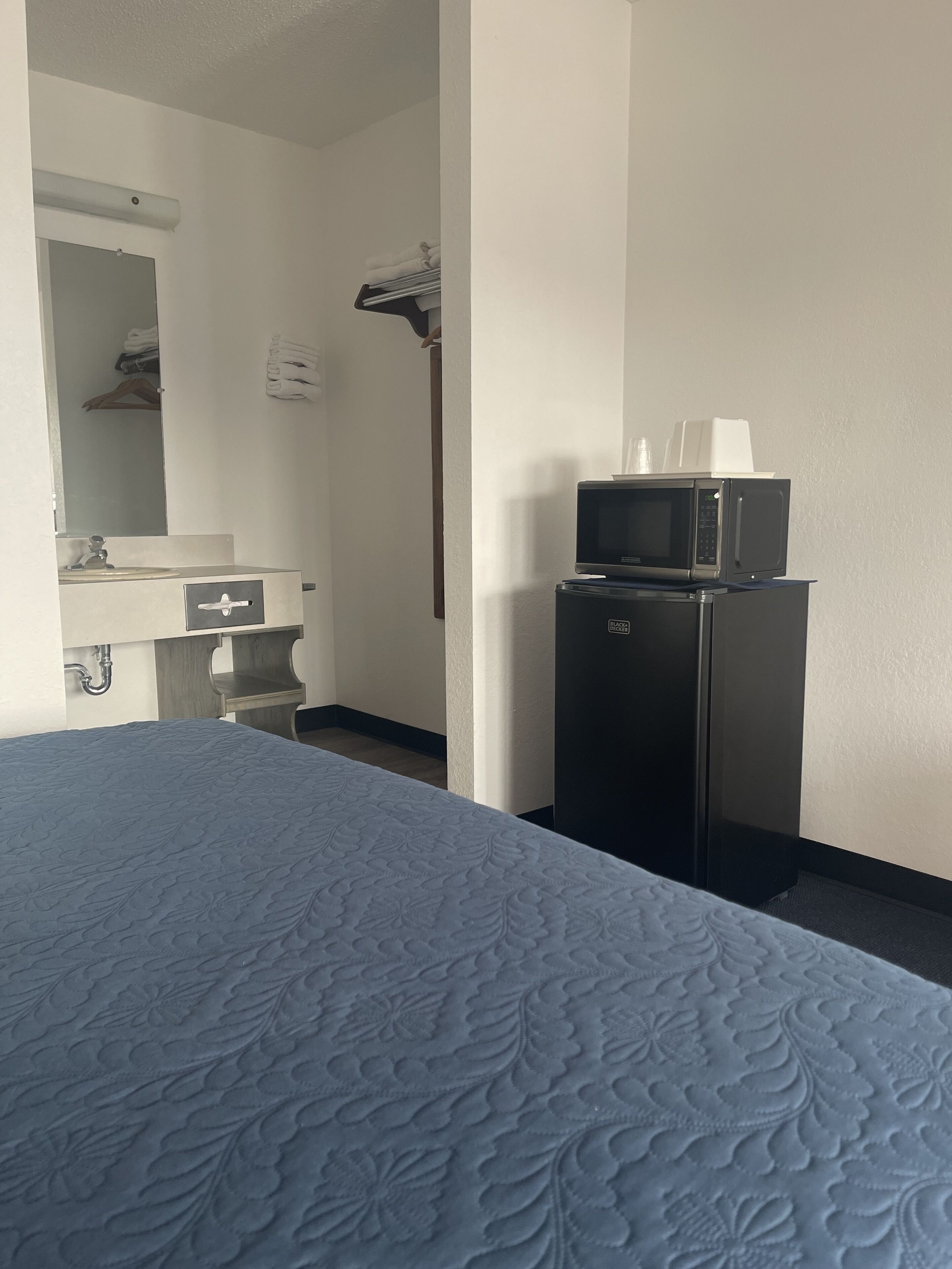 Une chambre d’hôtel équipée d’un lit, d’un petit bureau avec un miroir, d’un four à micro-ondes et d’un réfrigérateur.