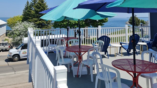 An outdoor seating area with tables and chairs, umbrellas, and a view of the sea. - Bayside Inn  (St Ignace)