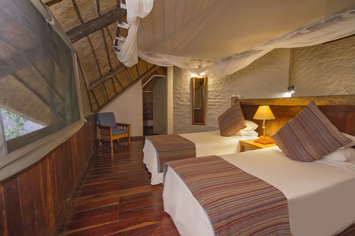 Une chambre avec deux lits, un plancher en bois, un mur en pierre et une fenĂȘtre.