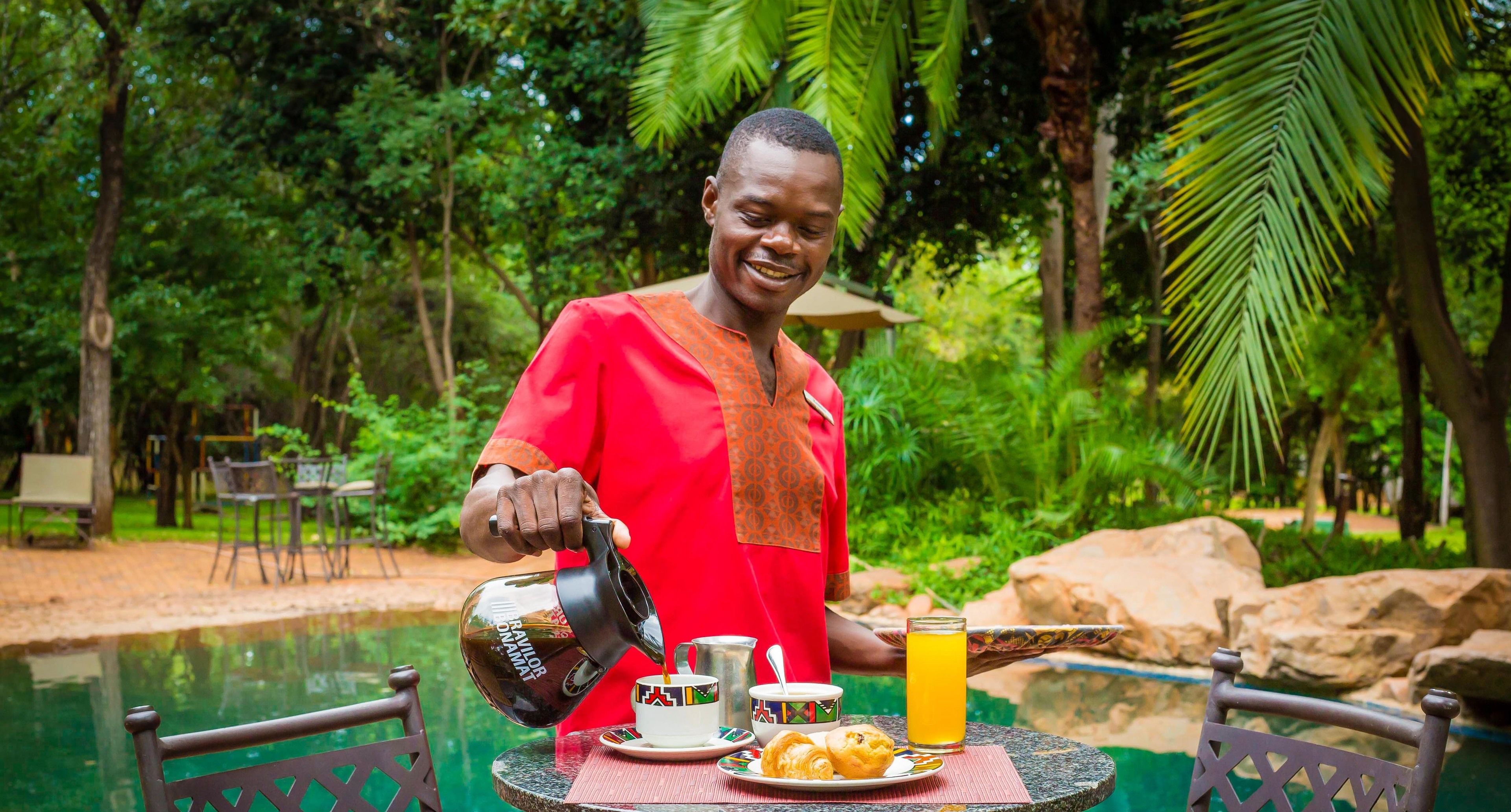 A person pouring coffee into a cup, sitting at a table with a plate of food and a glass of orange juice.