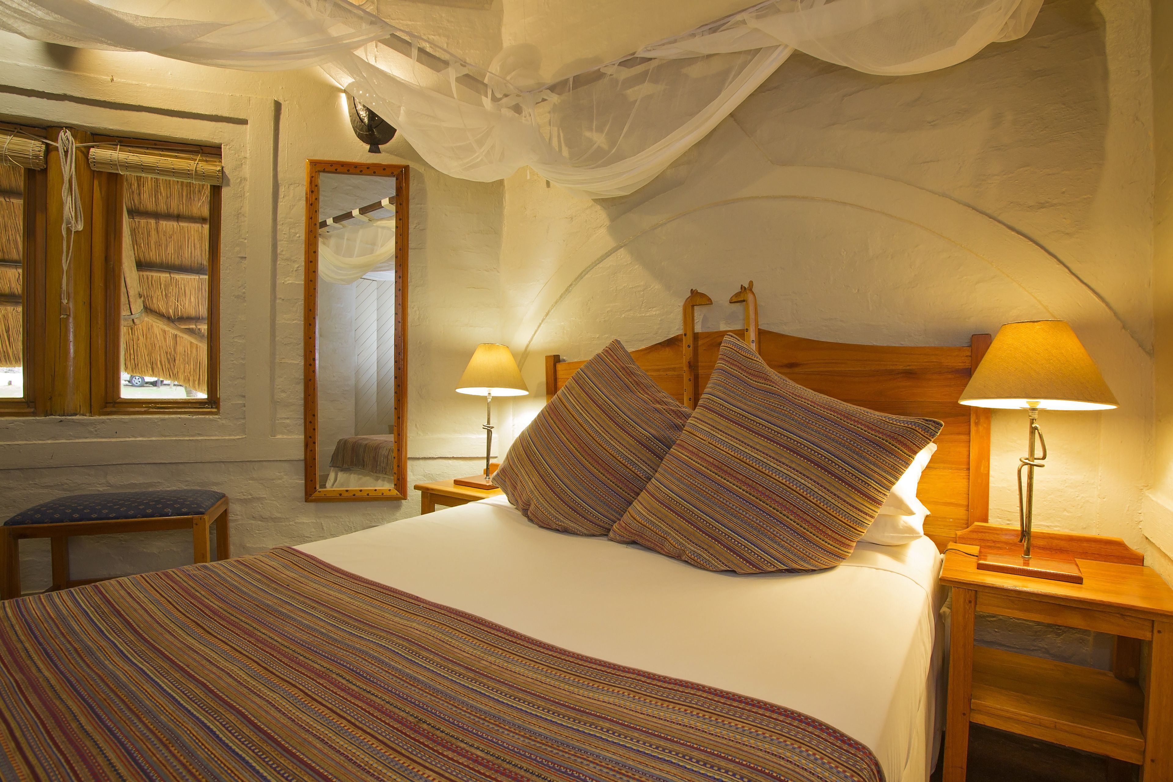 Een gezellige slaapkamer met een groot bed, twee bedlampjes, een houten hoofdeinde en een raam met gordijn.