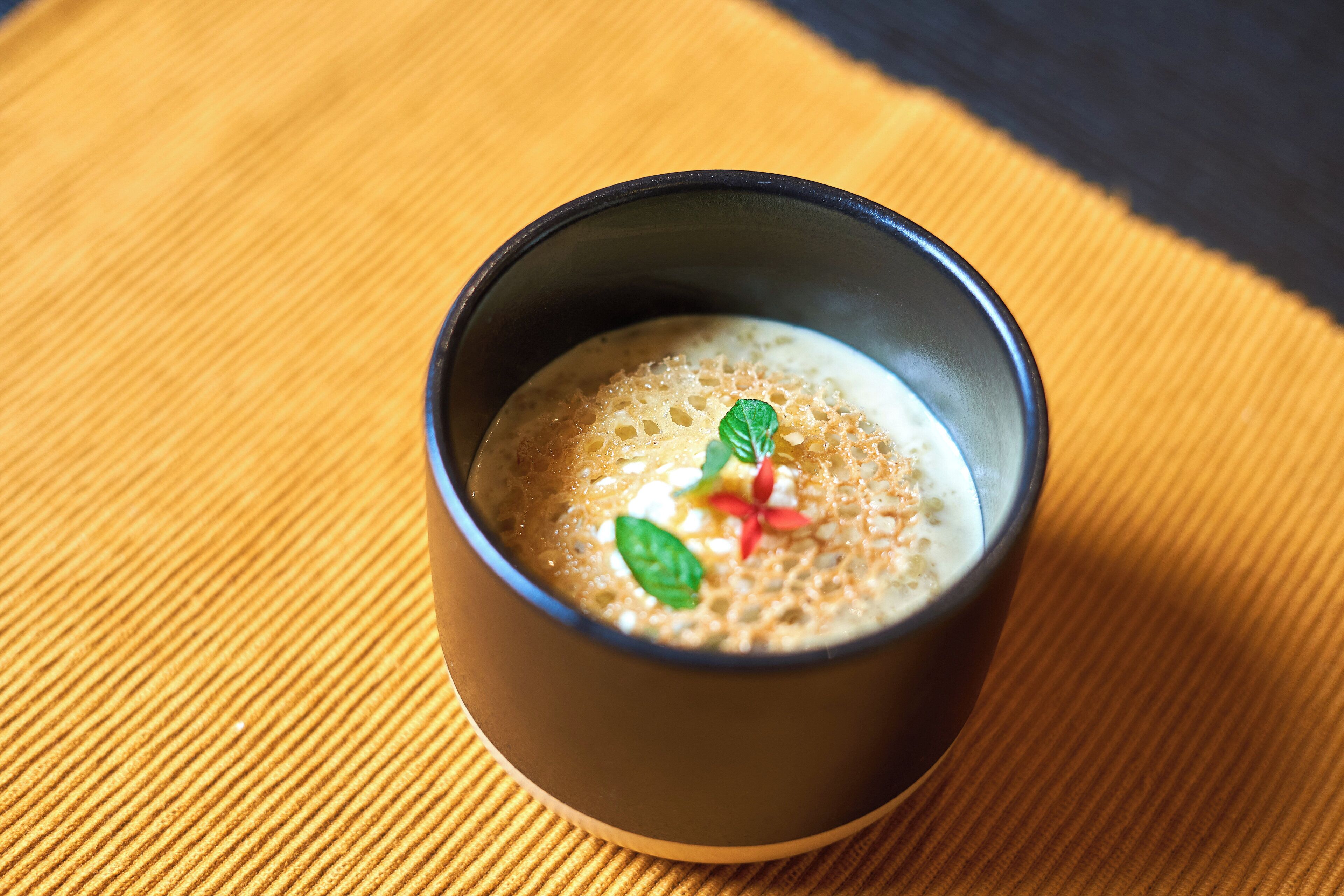 A cup of coffee with a frothy top and a mint leaf garnish on a wooden table.