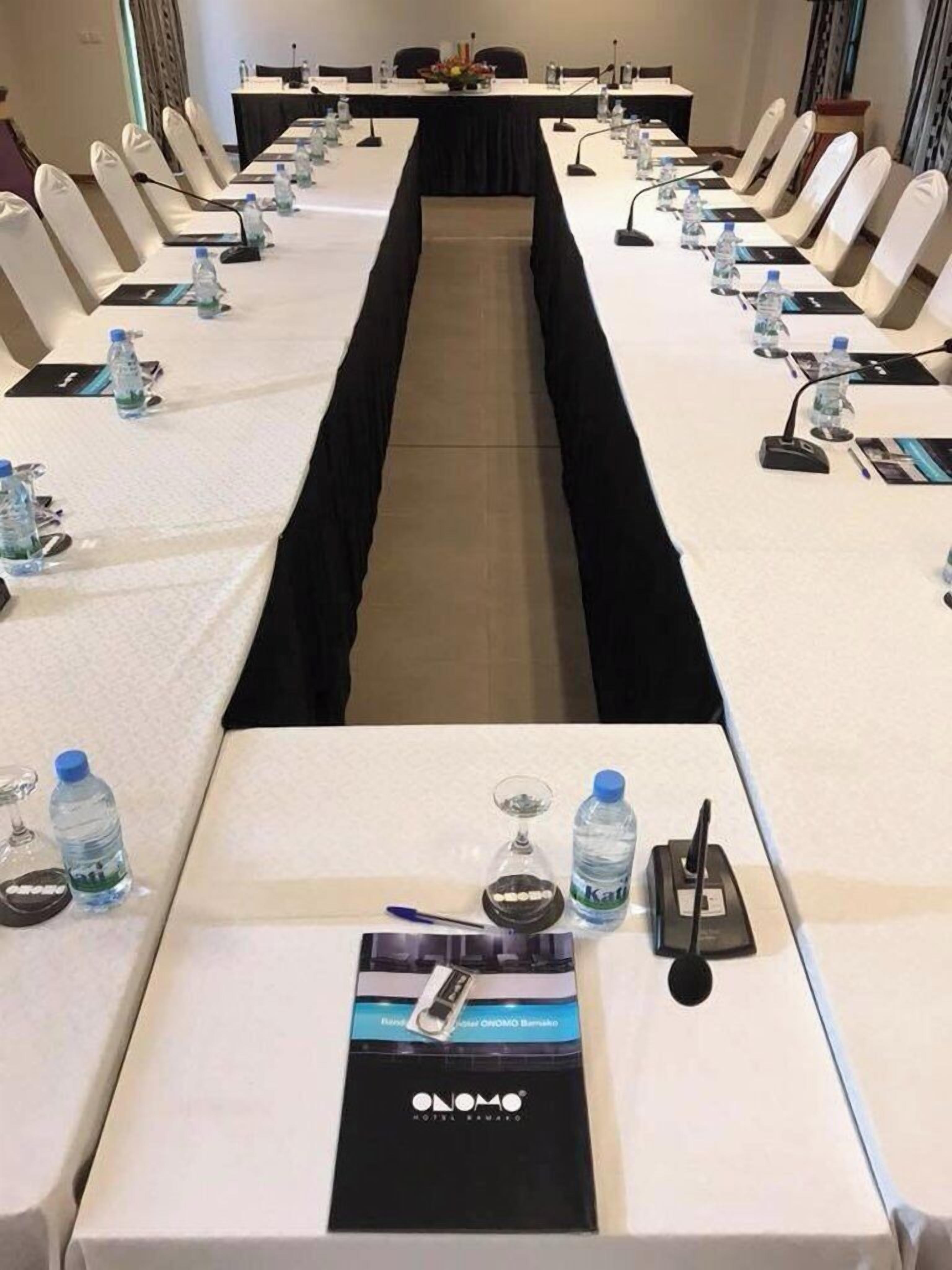 A conference room with a long table, chairs, water bottles, and a microphone.