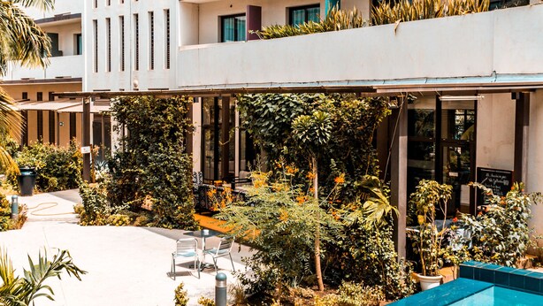 Un hotel moderno con piscina, mobiliario exterior y abundante vegetación.