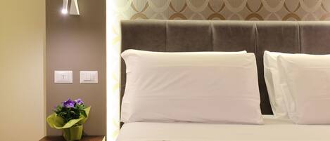 A hotel room with a bed, a nightstand with a vase of flowers, and a wall with a geometric pattern.