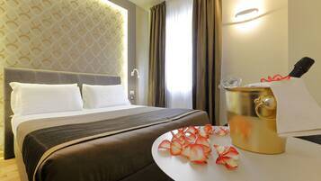 Una habitación de hotel con una cama, un minibar y una mesa con una botella y vasos.