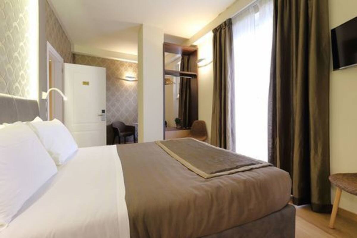 A hotel room with a large bed, a desk, a chair, and a TV mounted on the wall.