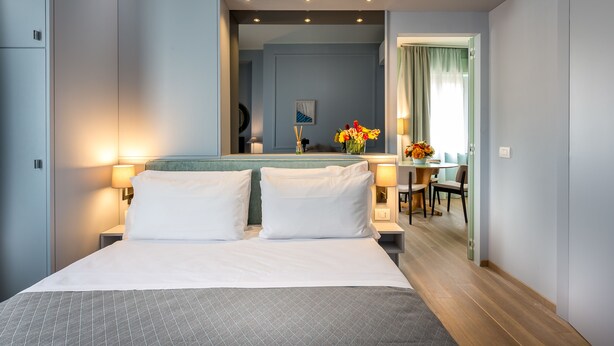 A hotel room with a large bed, bedside lamps, a mirror, a small table with a vase of flowers, and a view of the dining area. - La Torre Dei Salterelli (Florence)