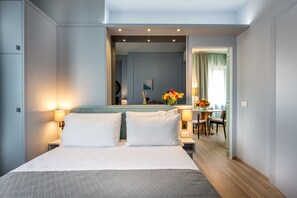 A hotel room with a large bed, bedside lamps, a mirror, a small table with a vase of flowers, and a view of the dining area. - La Torre Dei Salterelli (Florence)