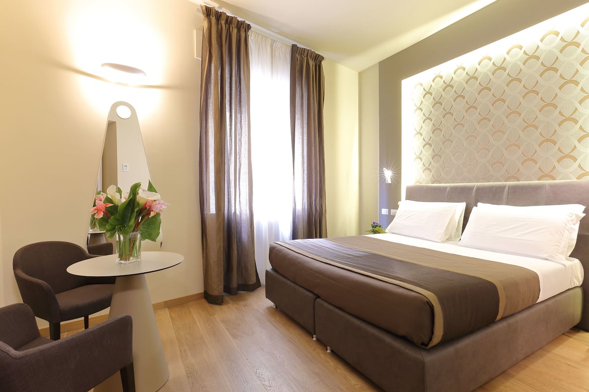 A hotel room with a bed, a desk, a chair, and a window with curtains.