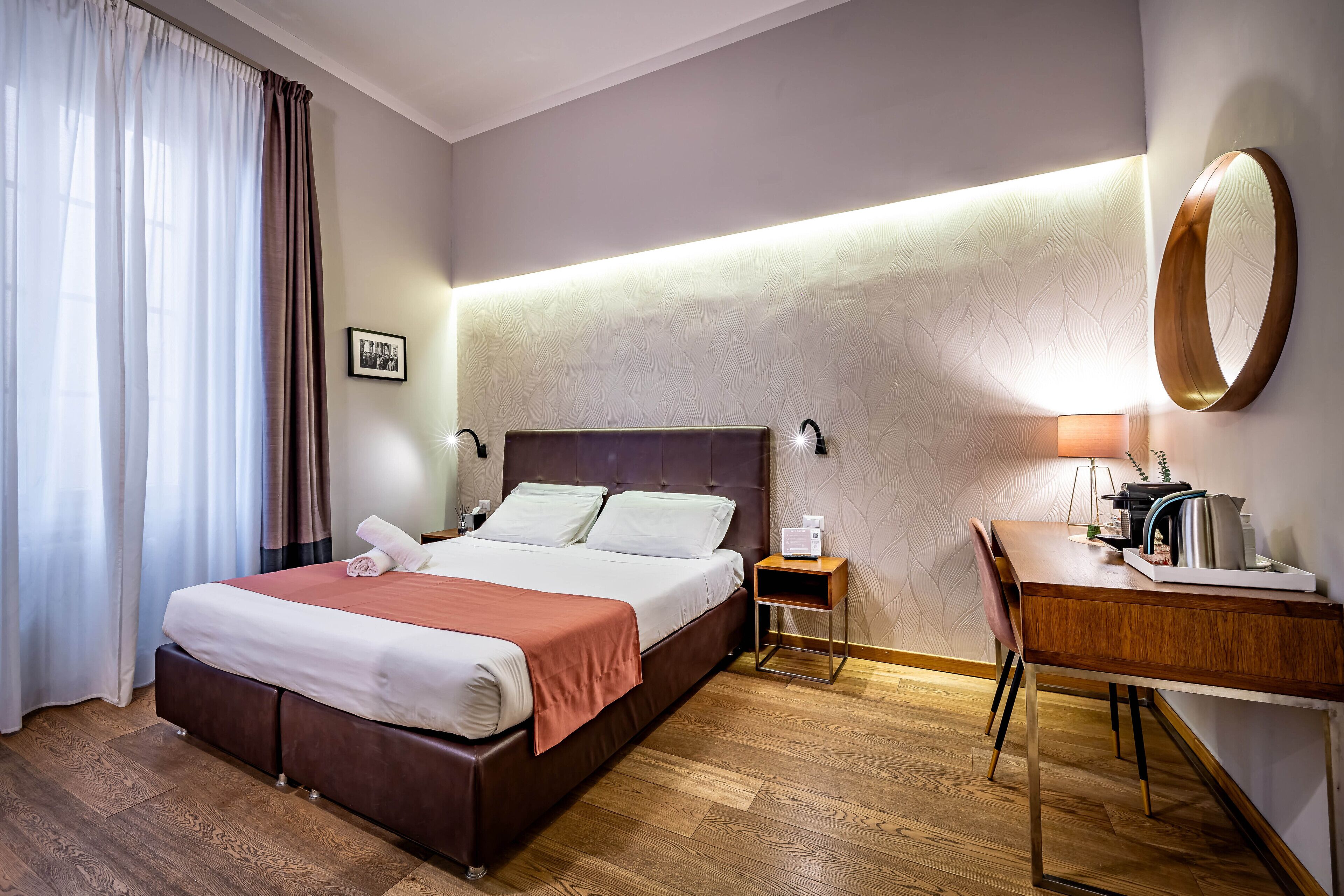 Ein Hotelzimmer mit Bett, Schreibtisch, Stuhl, Nachttisch und einer Wandlampe.