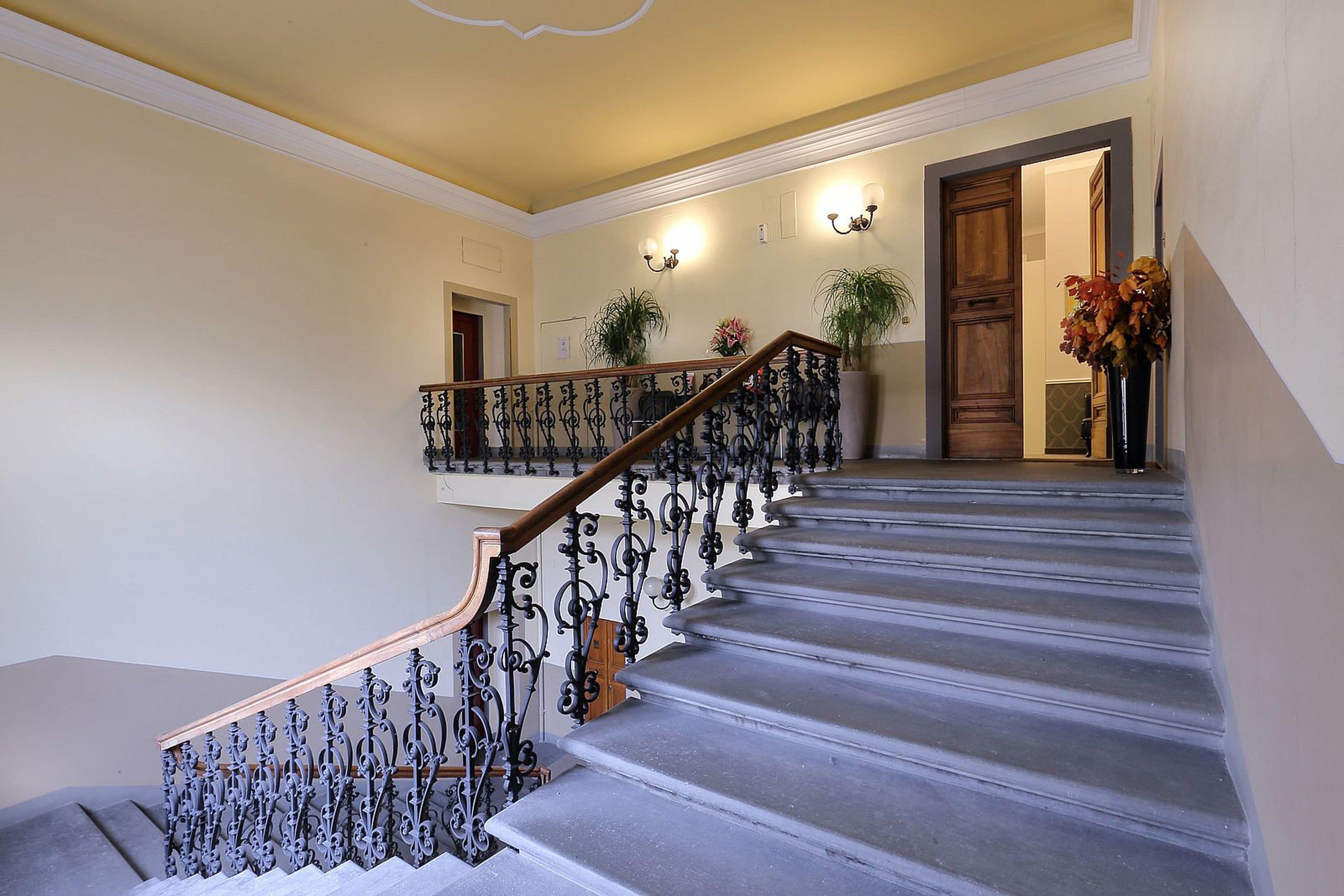 A grand staircase with ornate metal railings and a wooden handrail, leading to a landing with a door and a potted plant.
