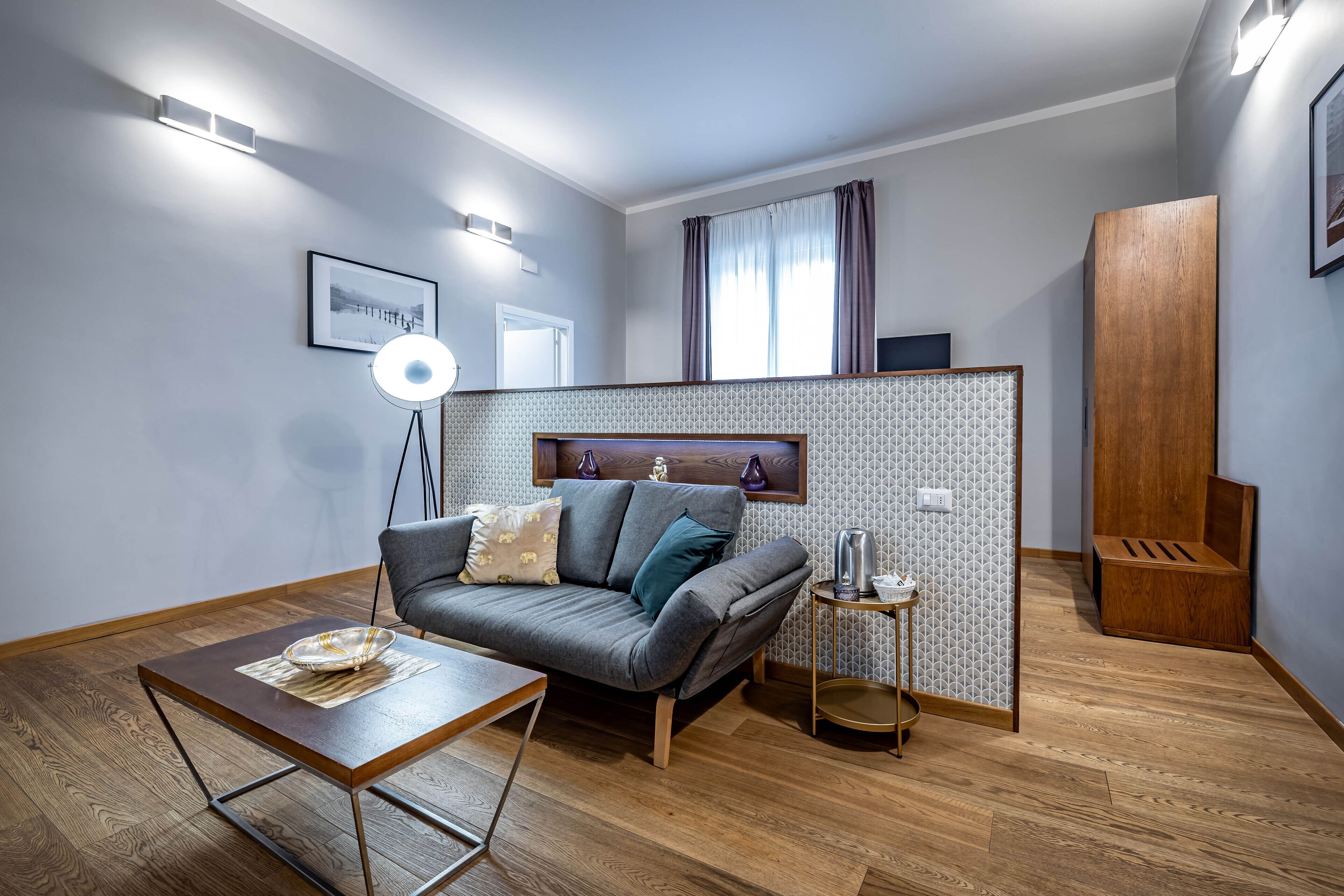 Una sala de estar moderna con un sofá gris, una mesa de centro, una lámpara de pie y un armario de madera.