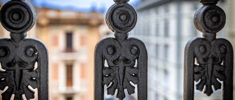 A wrought iron balcony railing with intricate designs, overlooking a building with classical architecture.