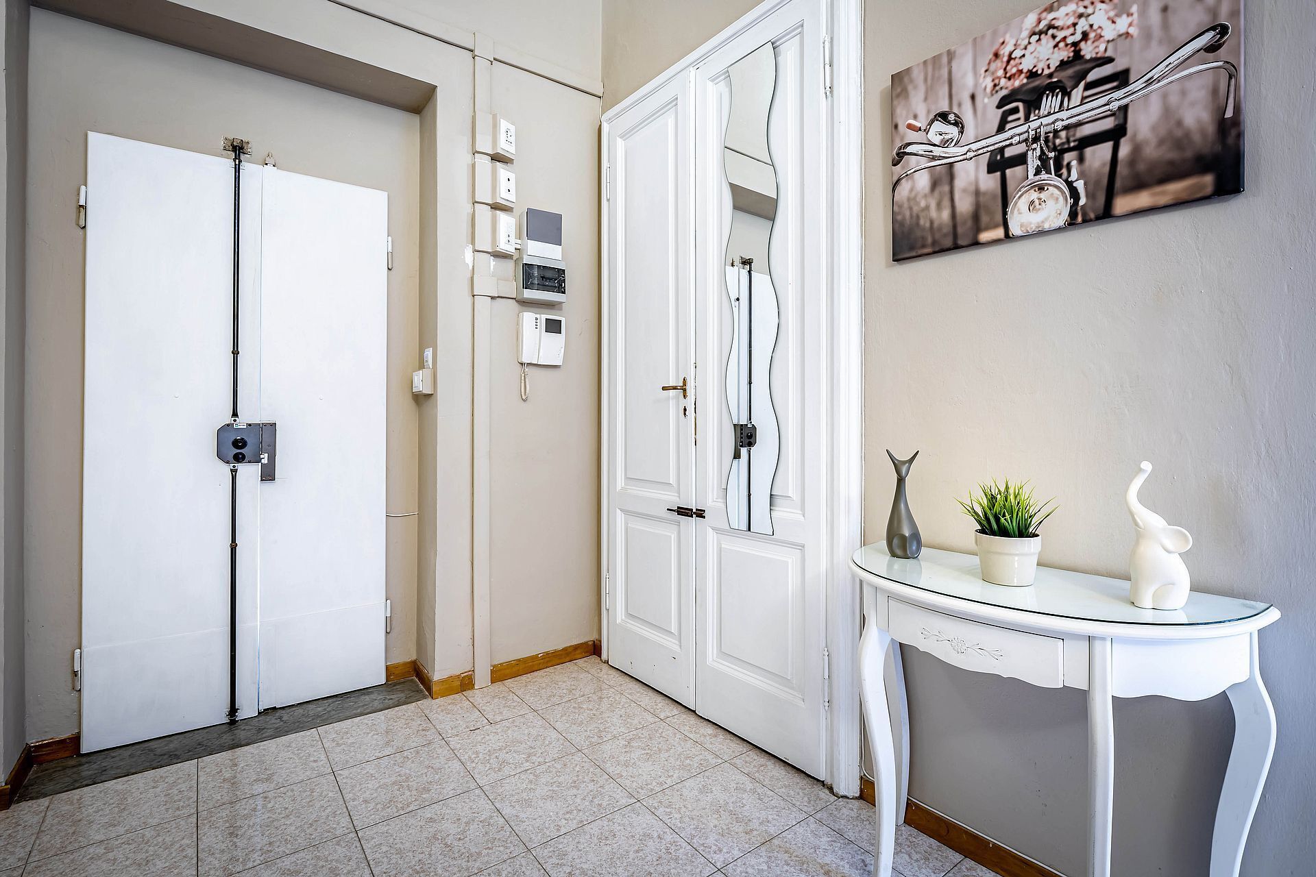 A hallway with white doors, a wall-mounted telephone, and a small table with a potted plant and decorative items.
