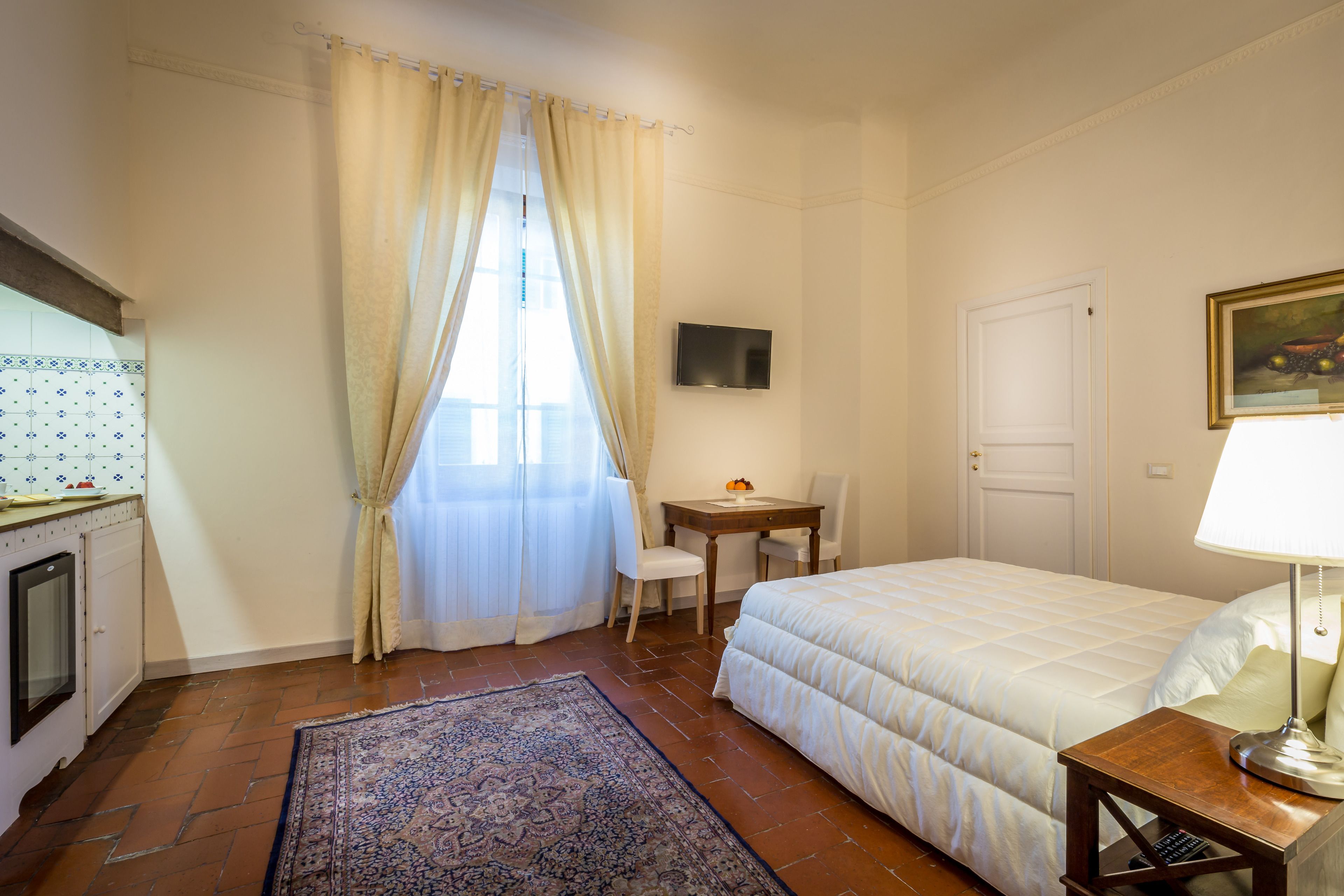 Une chambre à coucher avec un lit, un bureau, une chaise, une télévision et une fenêtre avec des rideaux.