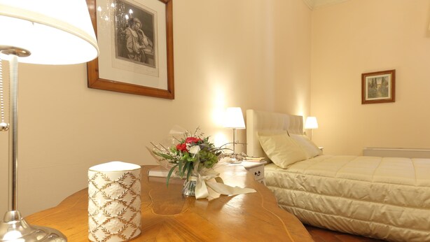 Habitación de hotel con una mesa de madera, una lámpara, un jarrón con flores, una cama y dos lámparas de noche.