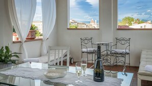 Un balcón con una mesa de vidrio, cortinas blancas y una botella de champán.