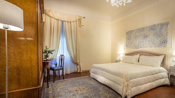 A bedroom with a large bed, a chandelier, a desk with a chair, and a large window with curtains.