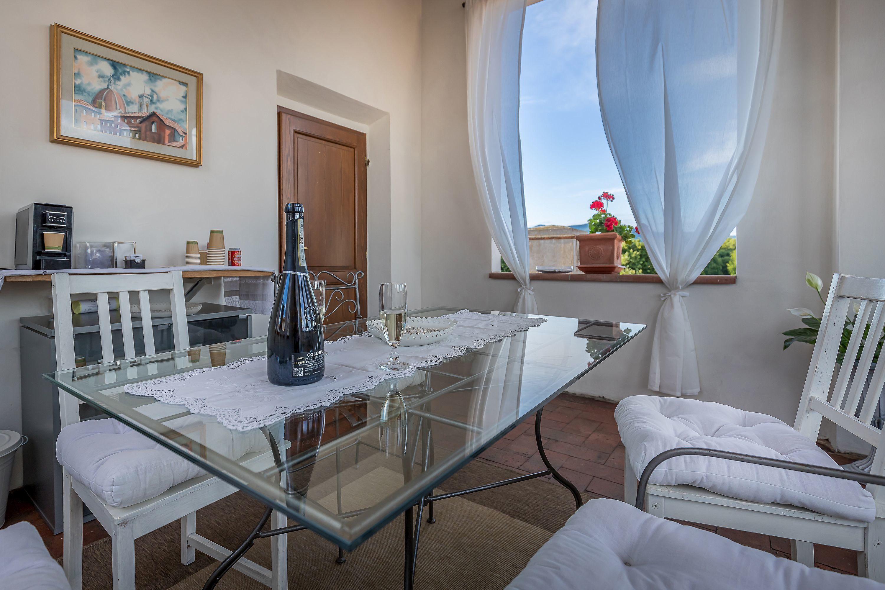 Un coin repas avec une table en verre, des chaises blanches, une machine à café et un tableau accroché au mur.