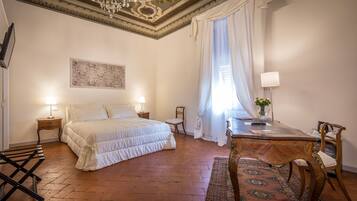 A bedroom with a large bed, a desk, a chair, a small table, a lamp, and a decorative rug.