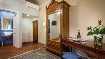 A room with a wooden dresser, a mirror, a blue chair, a small table with a vase of flowers, and a blue rug.