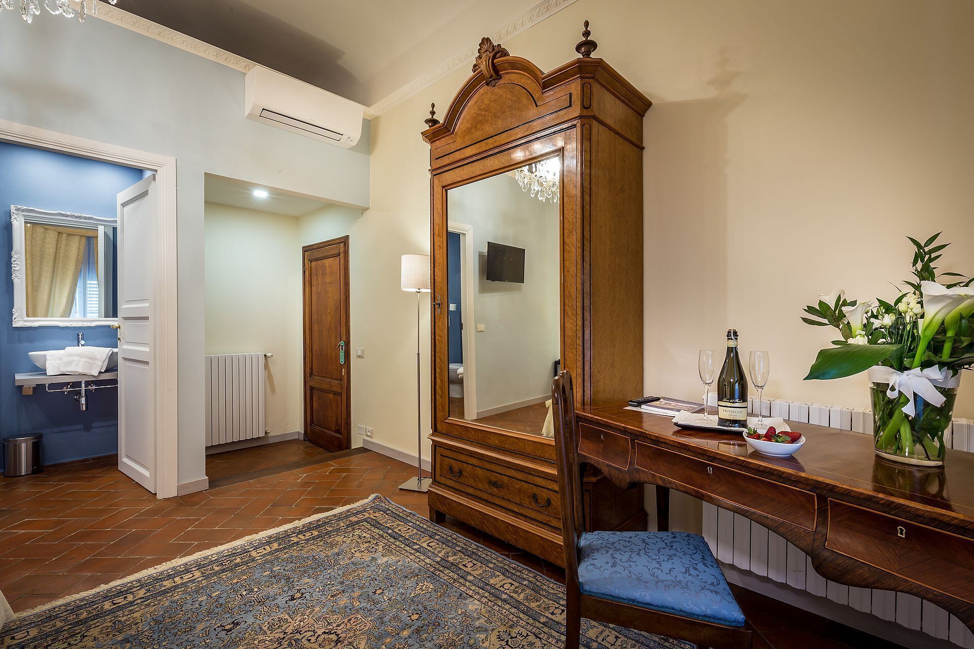 Ein Zimmer mit Holzschrank, Schreibtisch mit Stuhl, Spiegel, Heizkörper und Fernseher.