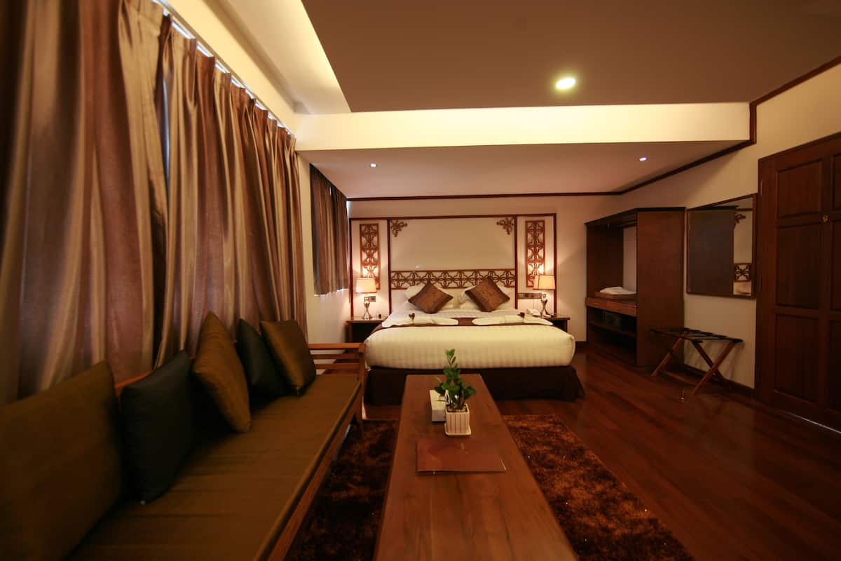 Une chambre d’hôtel avec un grand lit, un canapé, une table basse en bois et une petite table sur laquelle est posée une plante.