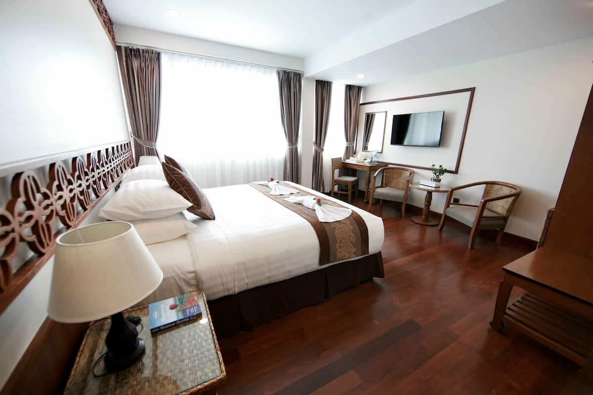 Une chambre d’hôtel avec un lit bien fait, un bureau, une chaise et un téléviseur fixé au mur.