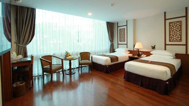 Quarto de hotel com duas camas, uma escrivaninha, uma cadeira, uma mesa pequena com abajur e uma janela grande com cortinas.