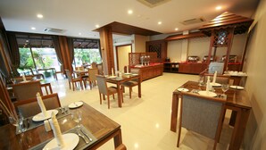 Uma área de refeições com mesas e cadeiras de madeira, um serviço de buffet e vista para o verde lá fora.