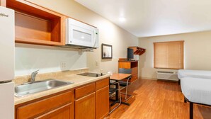 Una cocina compacta con armarios de madera, un microondas, un lavamanos y una pequeña zona de comedor con mesa y sillas.