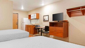 Habitación de hotel compacta con dos camas, kitchenette, televisor y un pequeño comedor.
