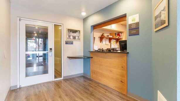 Zona de recepción con mostrador de madera, puerta de cristal y un cuadro en la pared.